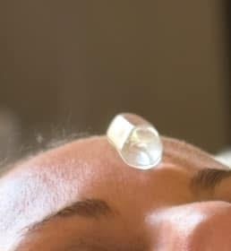 A clear quartz stone resting at the brow of a forehead, in soft warm light