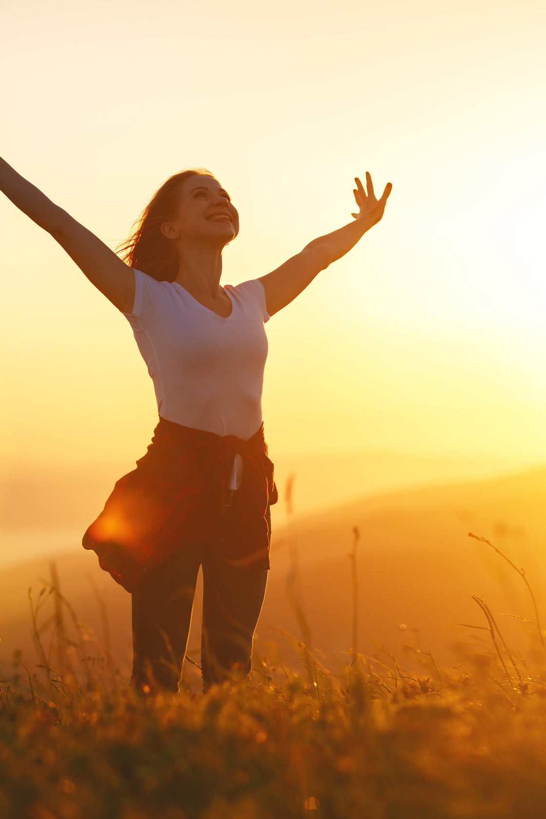 A woman standing in a golden sunset field with her arms raised joyfully to the sky, embodying the renewed vitality of the Life Activation