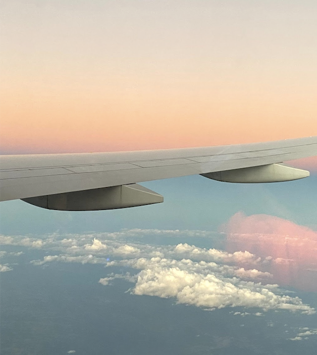 The wing of an aeroplane above clouds, with a peach and blue sunset sky beyond