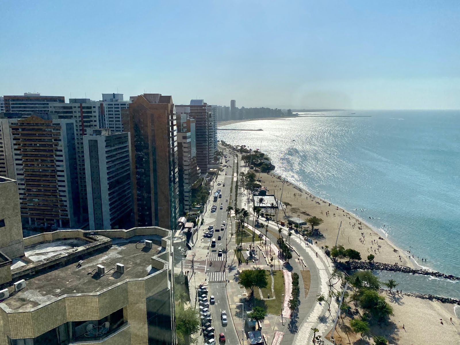 An aerial view of a Brazilian coastal city, high-rise buildings beside a palm-lined avenue and a wide beach