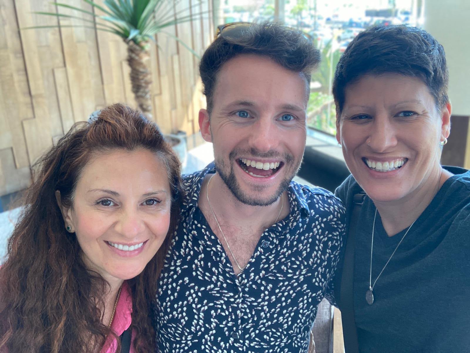 Three people smiling closely together for a photograph in warm daylight
