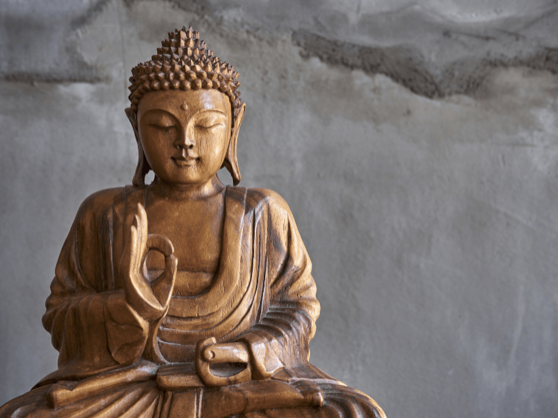 A carved wooden Buddha seated in serene meditation against a pale stone wall